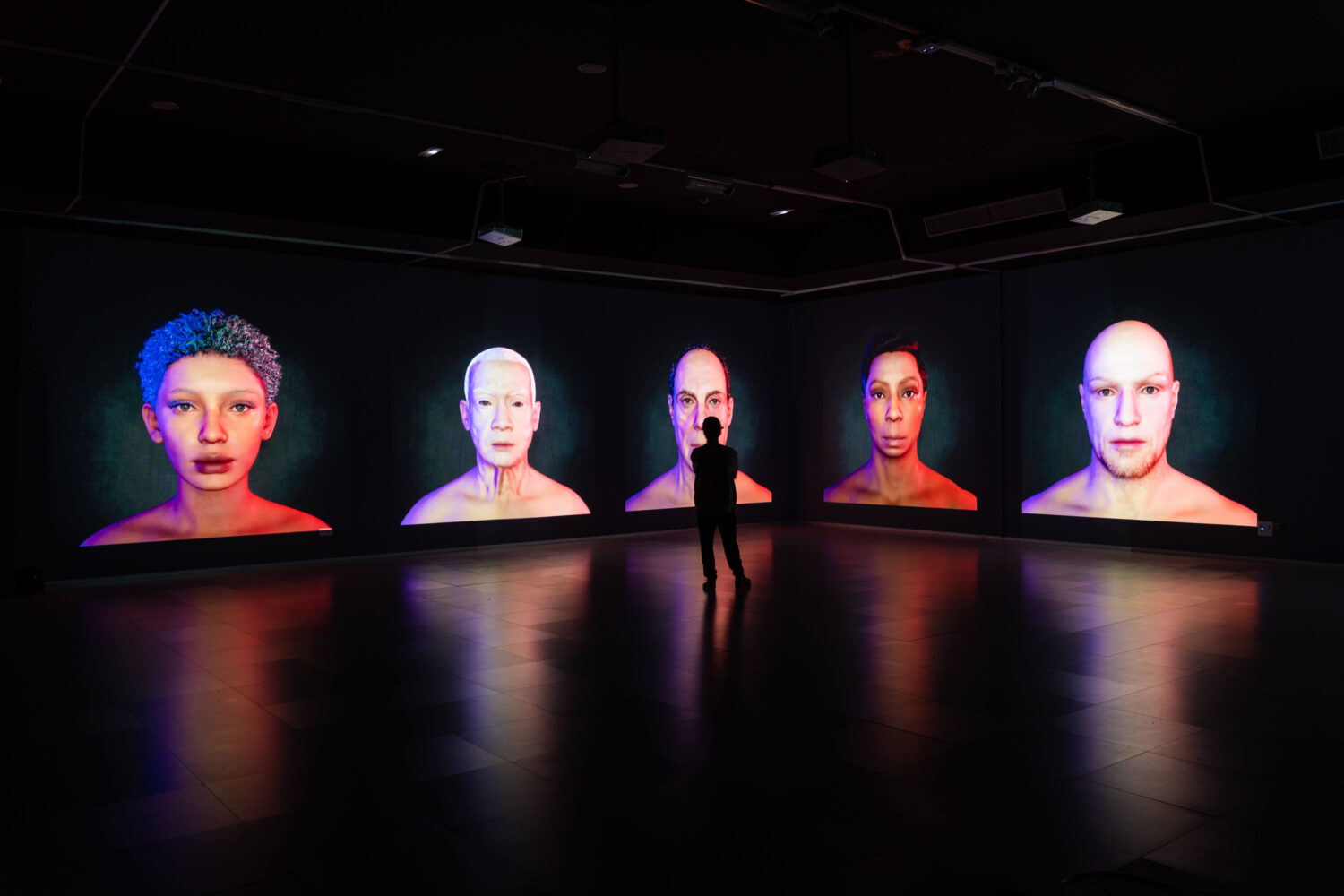 A visitor stands among five illuminated virtual faces in Călin Segal’s Whispers installation