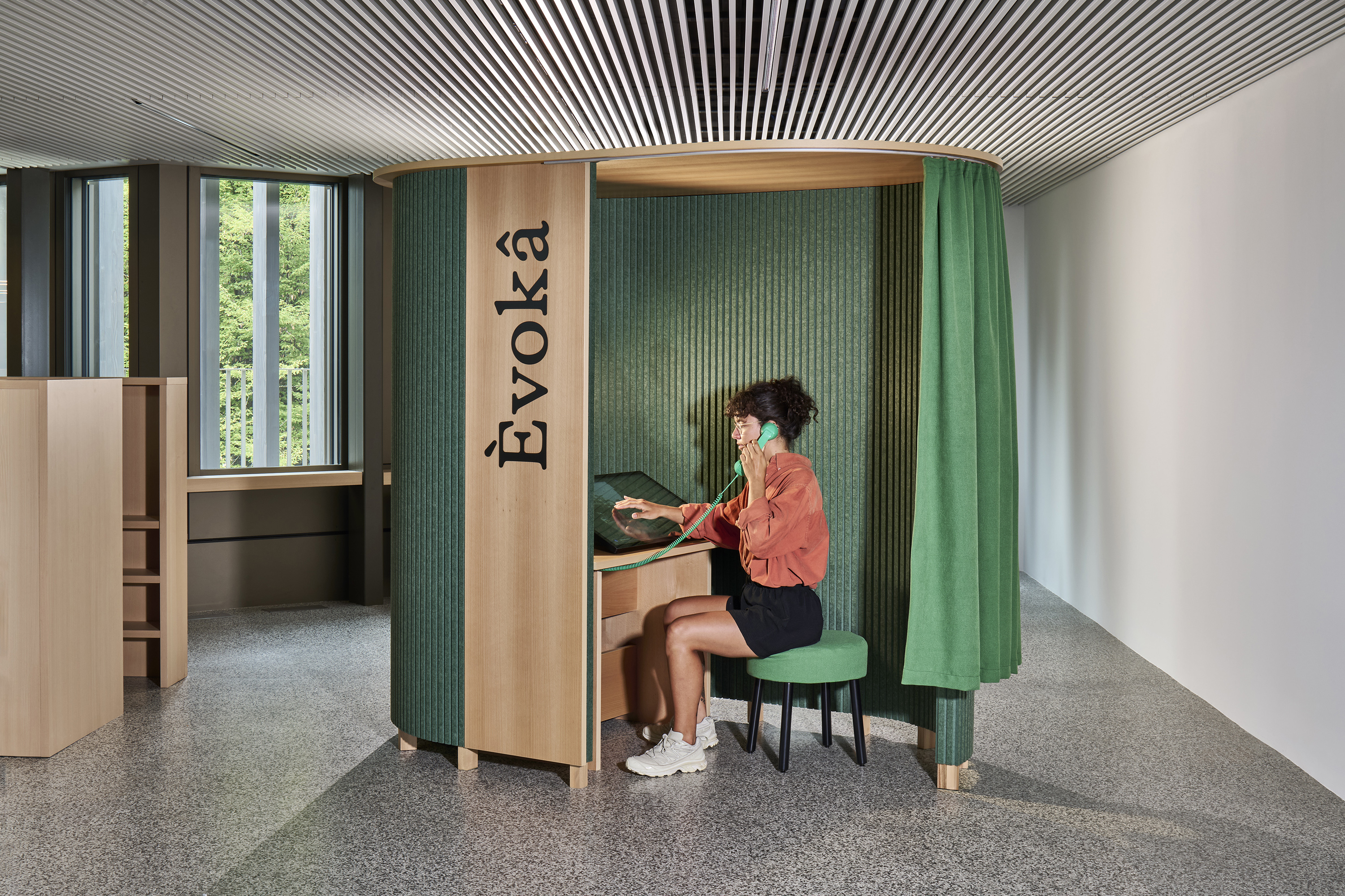 a visitor uses a green handset and touchscreen inside the wood-and-curtain èvokâ ii installation